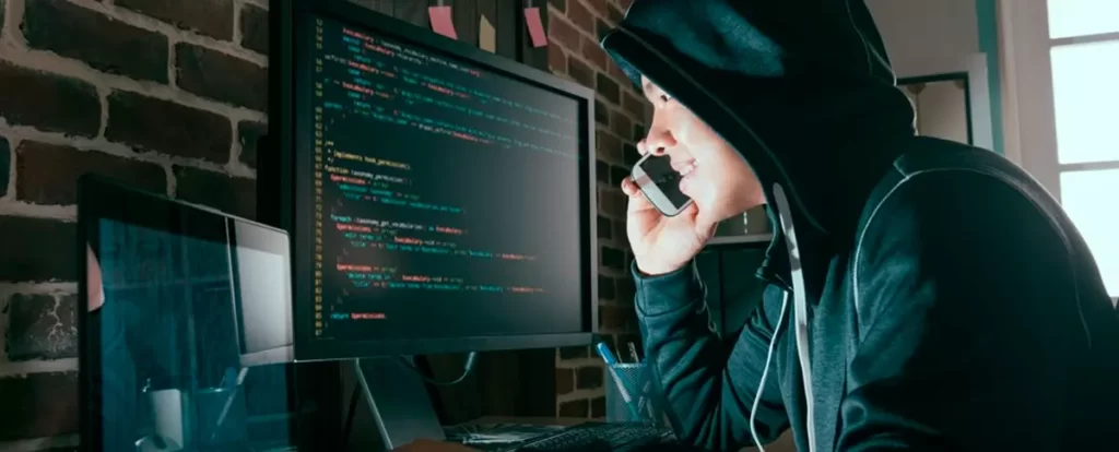 hacker fazendo uma ligação pelo celular e olhando a tela do computador