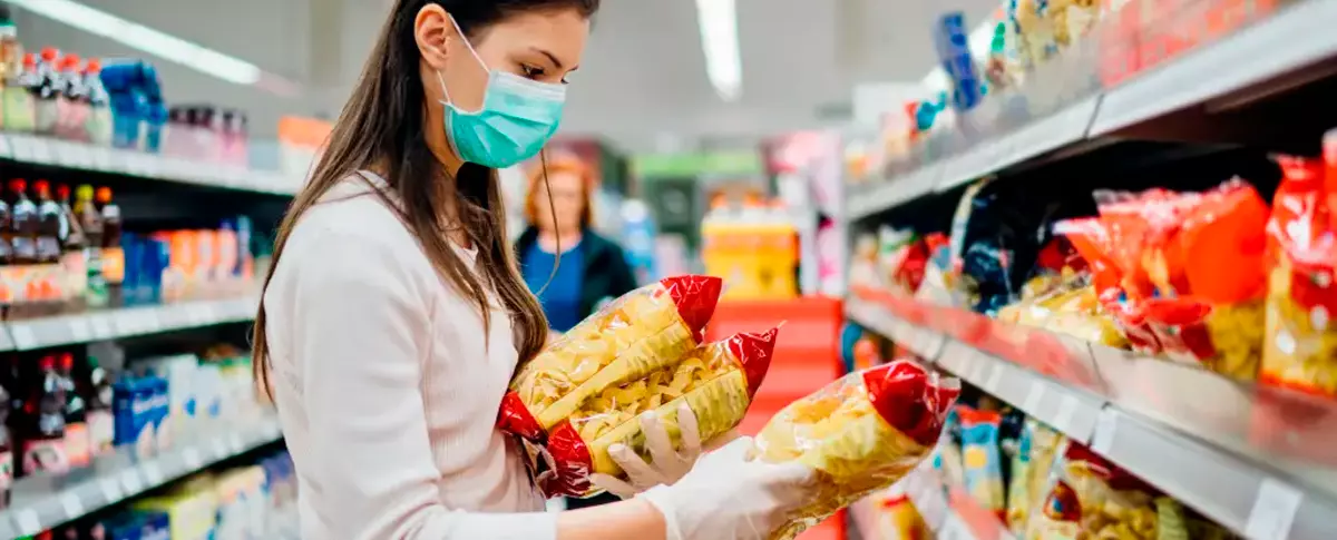 imagem de mulher no supermercado olhando para pacotes de macarrão que estão nas mãos