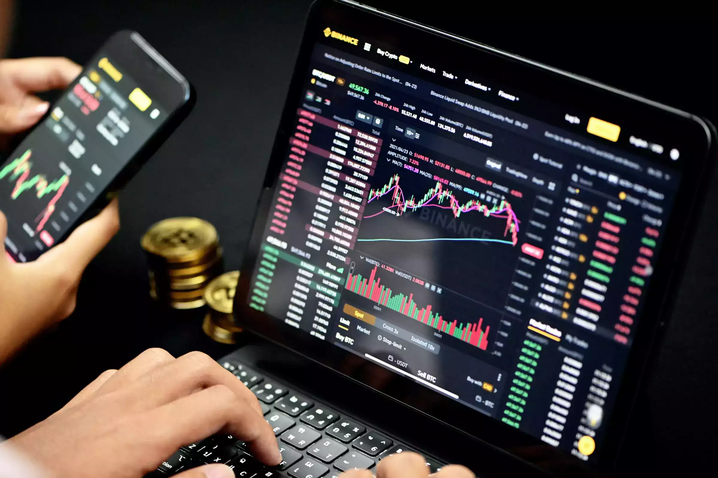 uma pessoa no notebook com gráfico bitcoin e uma pessoa com gráfico no celular