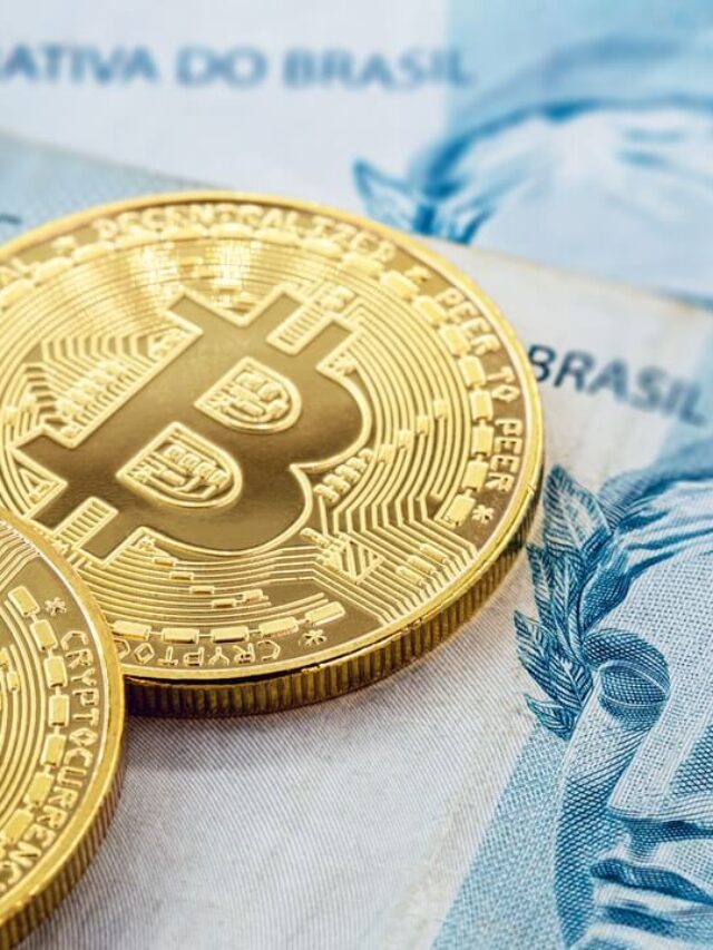 Imagem de notas de cem reais em baixo de moedas de Bitcoin
